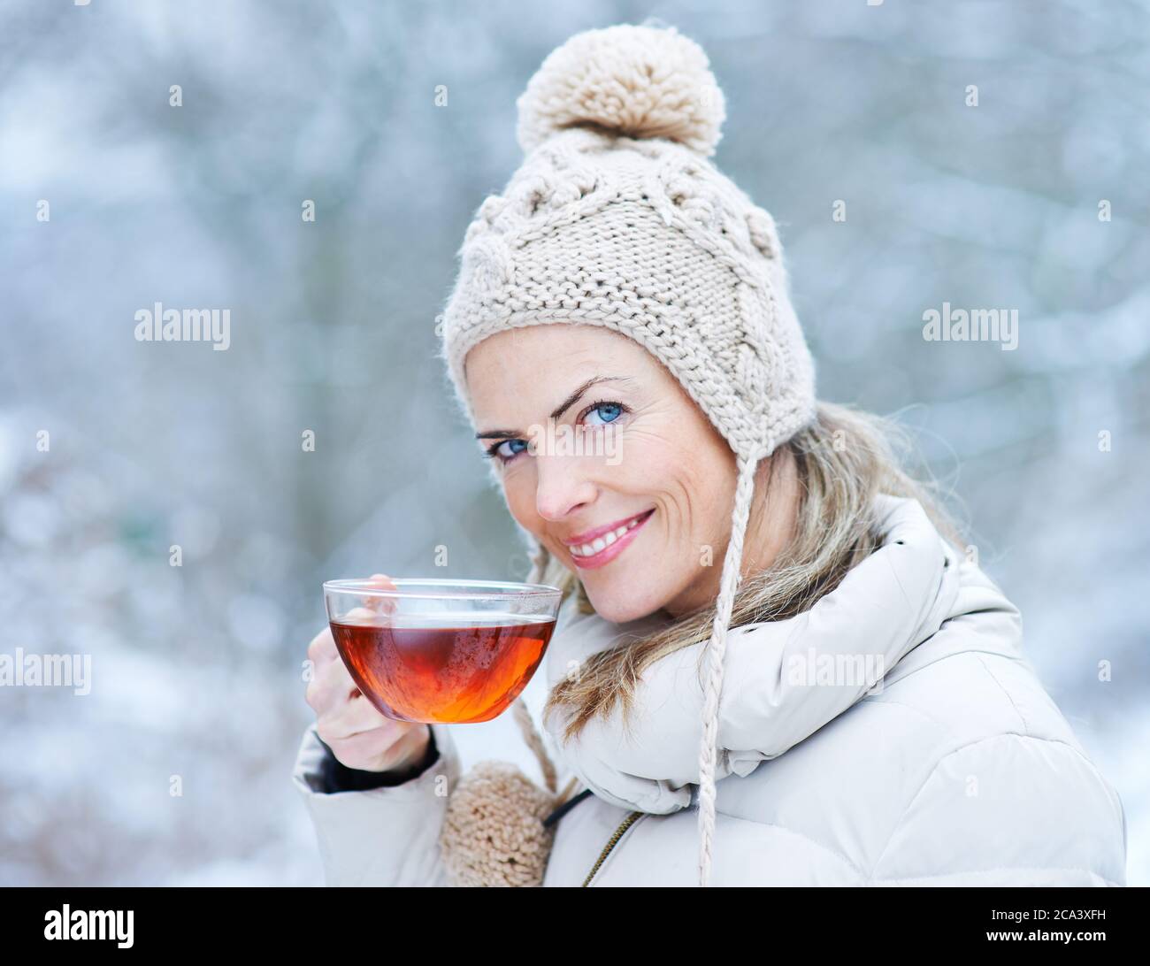 Donna sorridente beve una tazza di tè nero in inverno Foto Stock