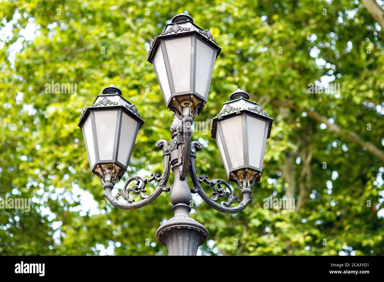 lampada da strada in stile retrò di ferro con motivi in ferro battuto e  sfumature di vetro, primo piano di lanterne in background alberi verdi Foto  stock - Alamy