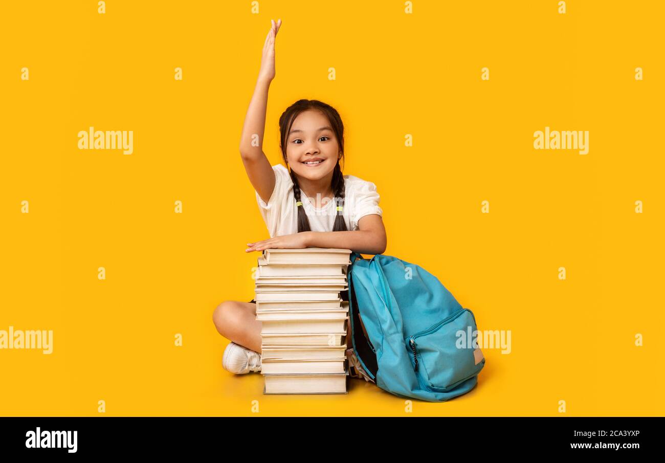 Ragazza della scuola che alza la mano seduta a Book Stack, Studio Shot Foto Stock