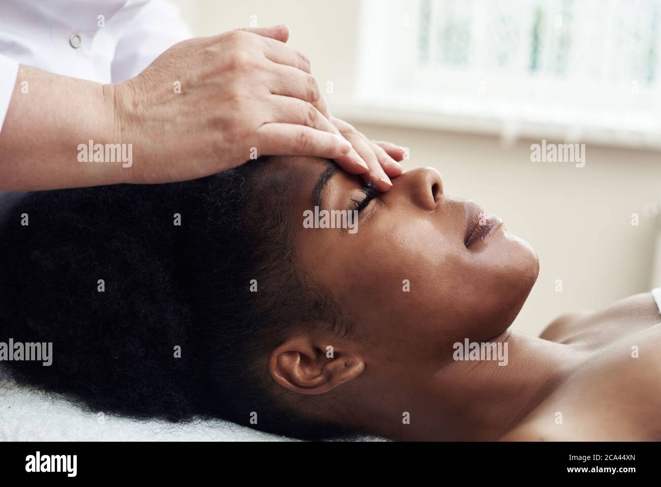 Una giovane donna nera si trova nell'ufficio dell'estetista e si distende dai tocchi delicati e dal massaggio tonificante. Il concetto di trattamenti spa. Foto Stock