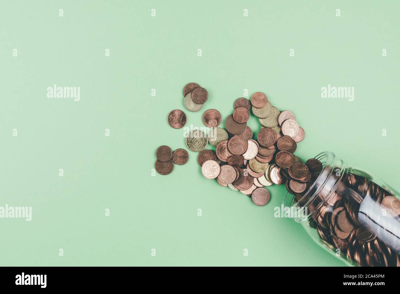 Sopra la vista di piccole monete euro cambio che fuoriescono dal vaso di vetro su sfondo verde Foto Stock