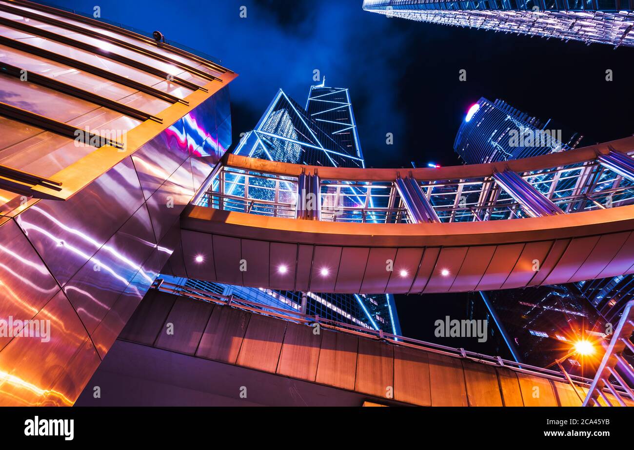 Moderno paesaggio urbano di notte con grattacieli illuminati e ponti a piedi. Alti edifici aziendali della città di Hong Kong Foto Stock