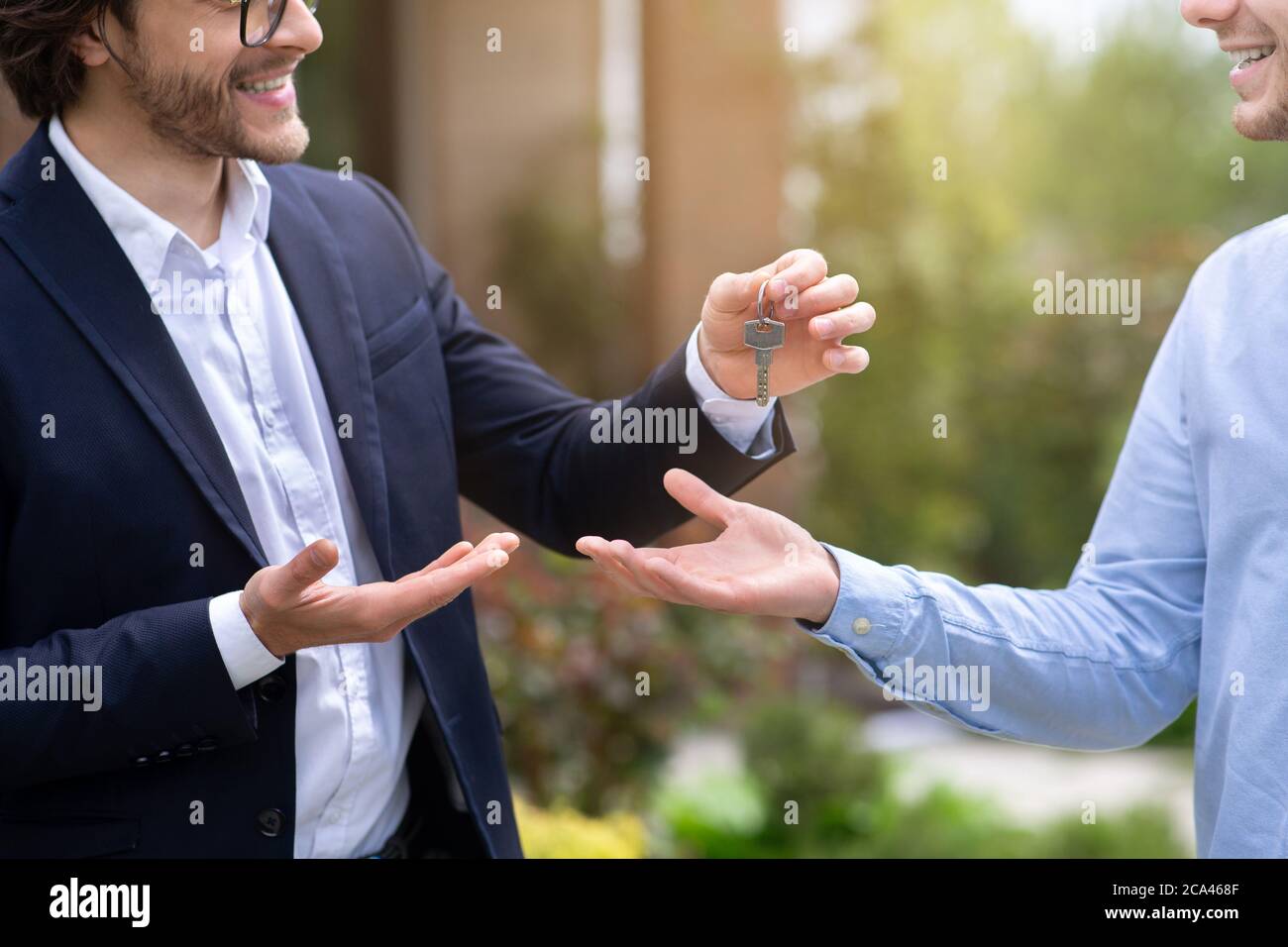 Vista ritagliata dell'agente immobiliare che dà la chiave della casa al nuovo proprietario della casa vicino alla sua proprietà, primo piano Foto Stock