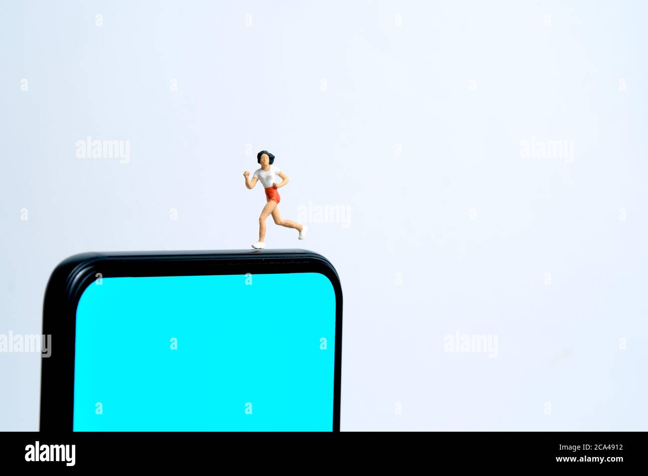 Concetto di app per il monitoraggio della corsa e del jogging. Una donna che corre sopra lo smartphone. Fotografia di figure di persone in miniatura. Foto Stock