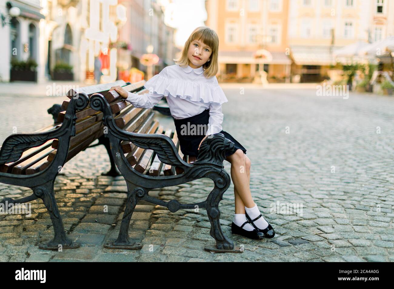 Concetto di moda di strada per bambini. Bella bambina in camicia bianca e gonna  nera seduta sulla panca vintage nella città vecchia all'aperto Foto stock -  Alamy