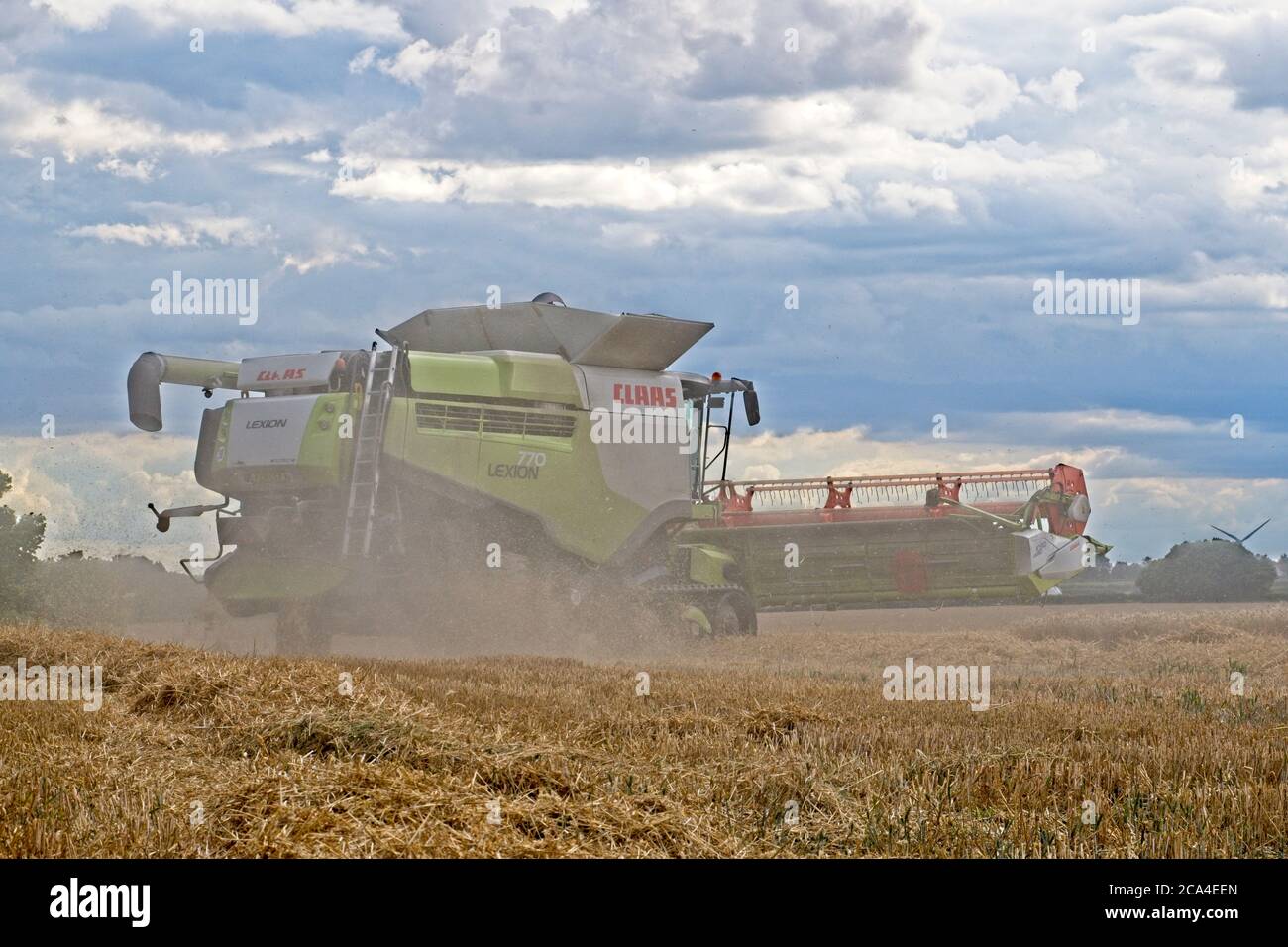 Raccolta invernale Vista laterale ravvicinata della macchina combinata della trebbiatrice Lavoro nel campo raccolta raccolto cielo nuvoloso polvere volo Paesaggio formato Foto Stock