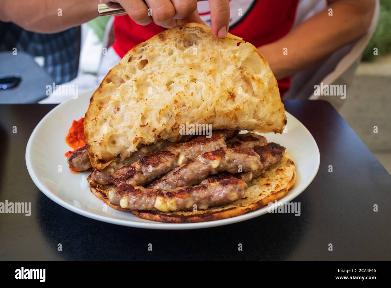 Cevapcici o cevapi, piatto bosniaco preparato al barbecue e servito con pane Lepinja. Piatto popolare balcanico. Foto Stock