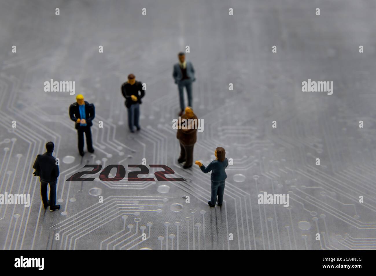 Figurine in miniatura poste come uomini d'affari in una riunione su circuito stampato futuristico astratto con l'anno di testo 2022 Foto Stock