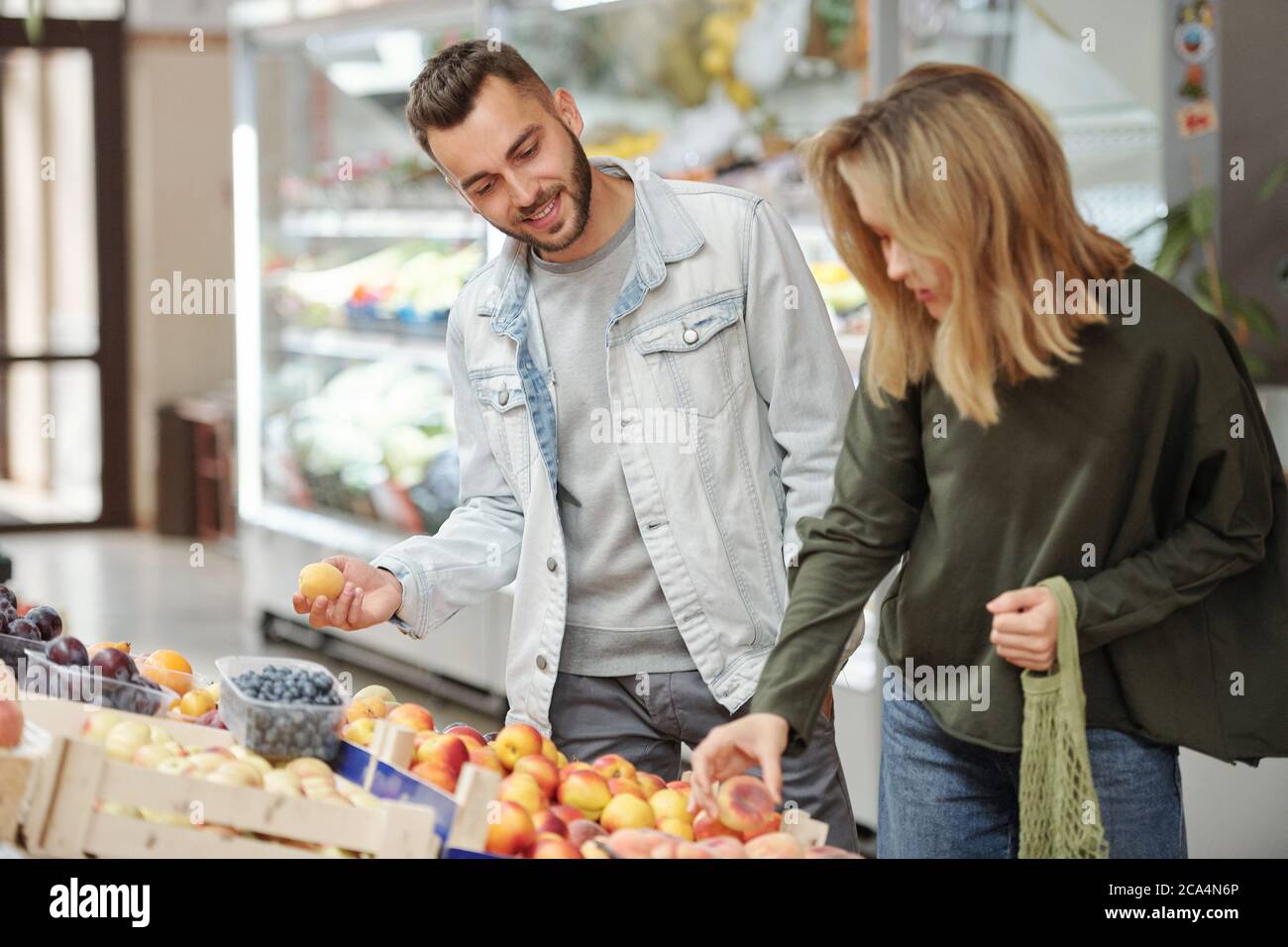 Soddisfare giovane coppia in abiti casual in piedi al bancone del cibo e alla ricerca di frutta matura al mercato agricolo Foto Stock