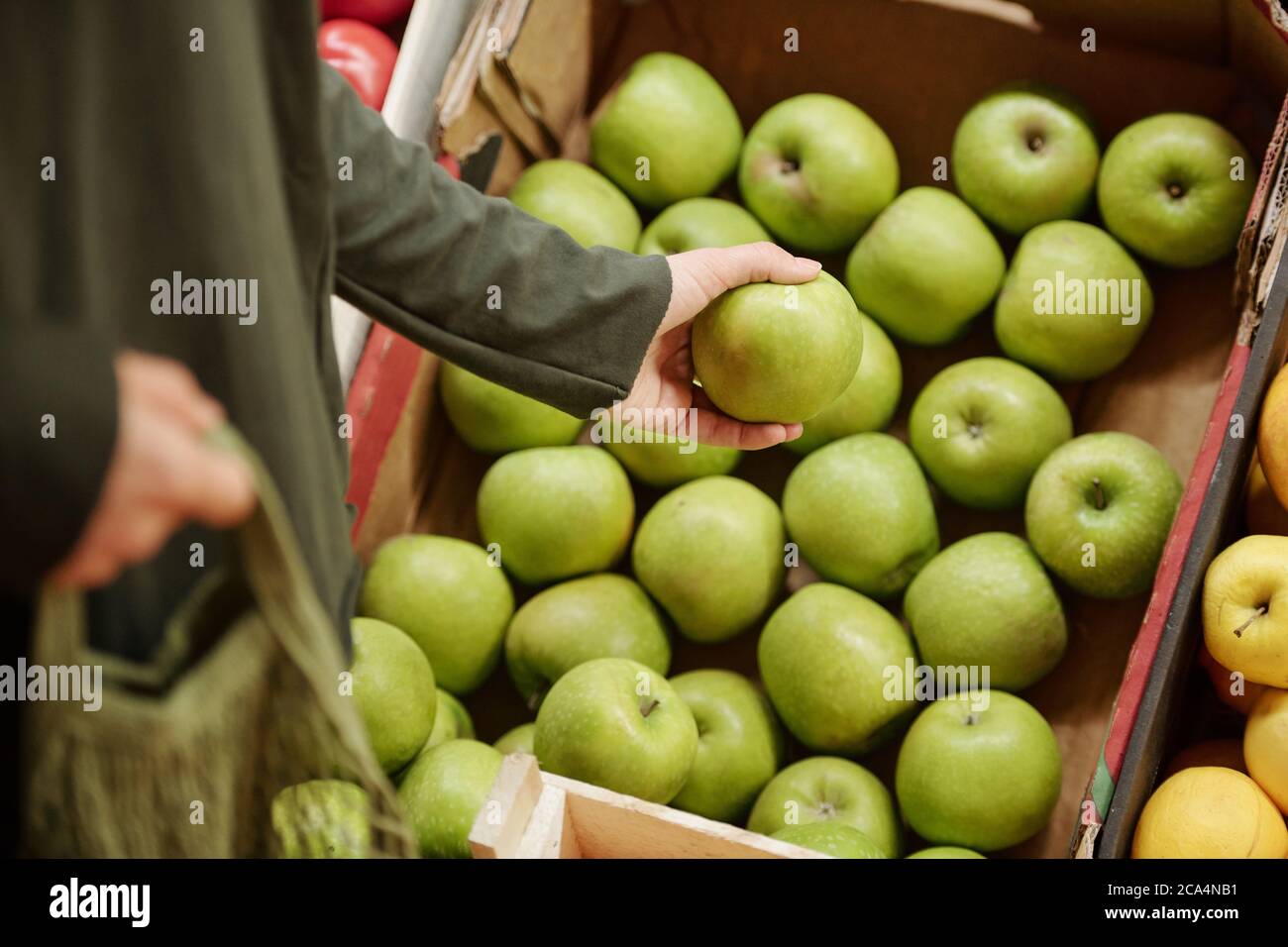Primo piano del cliente irriconoscibile che si trova al banco e sceglie le mele verdi nella scatola Foto Stock