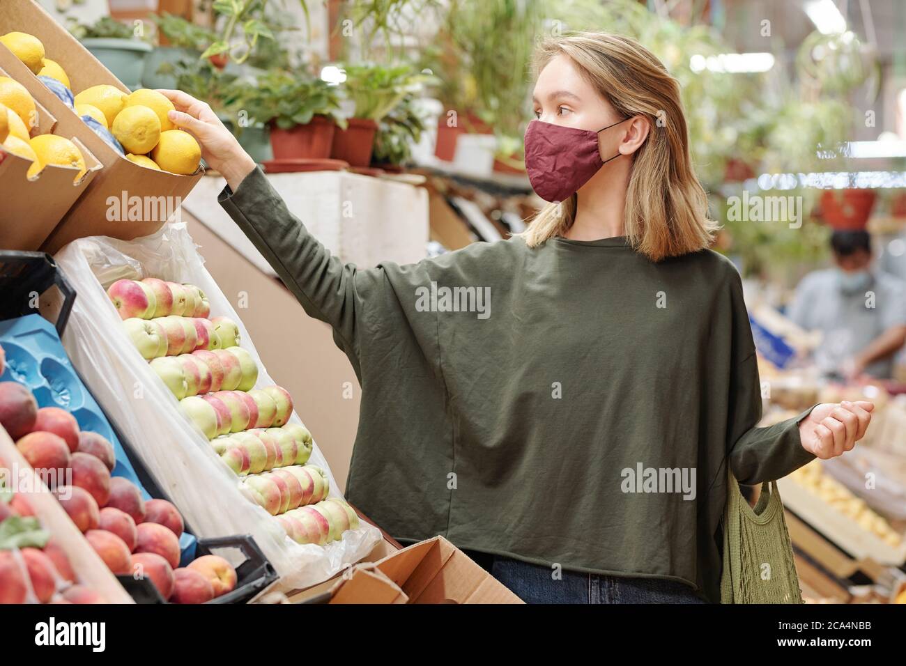 Attraente giovane donna in maschera in piedi al banco e lo shopping per i generi alimentari durante il coronavirus Foto Stock