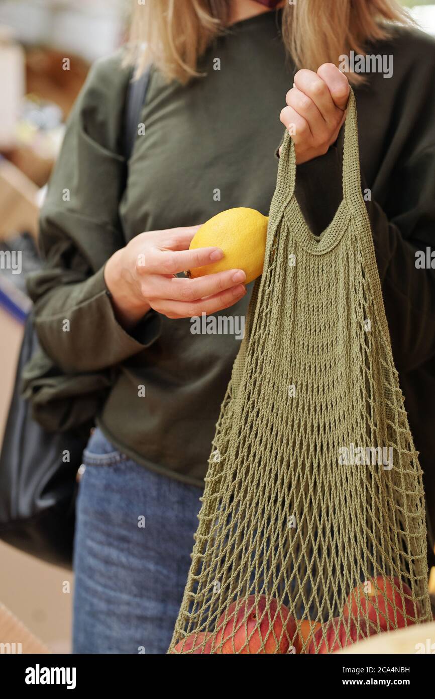 Primo piano di donna irriconoscibile che mette il limone in borsa della rete mentre lo acquista al mercato alimentare Foto Stock