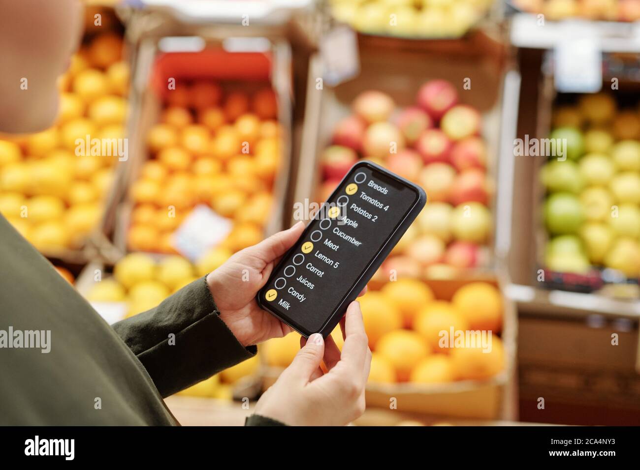 Vista a spalla della donna che legge l'elenco dei prodotti alimentari sullo smartphone mentre effettua acquisti al mercato alimentare biologico Foto Stock
