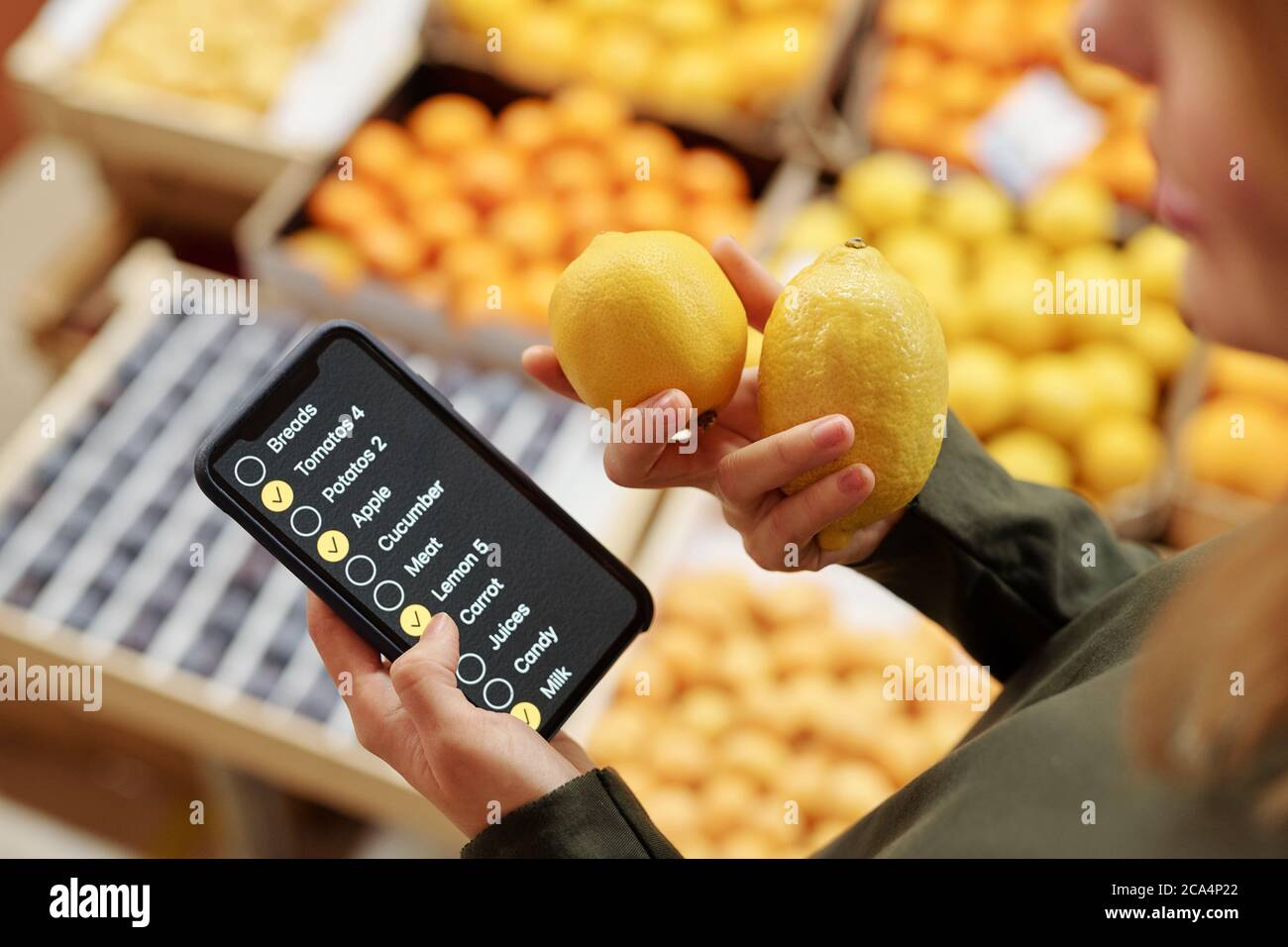 Primo piano di donna che usa la lista di controllo sullo smartphone nel supermercato mentre acquista i limoni Foto Stock