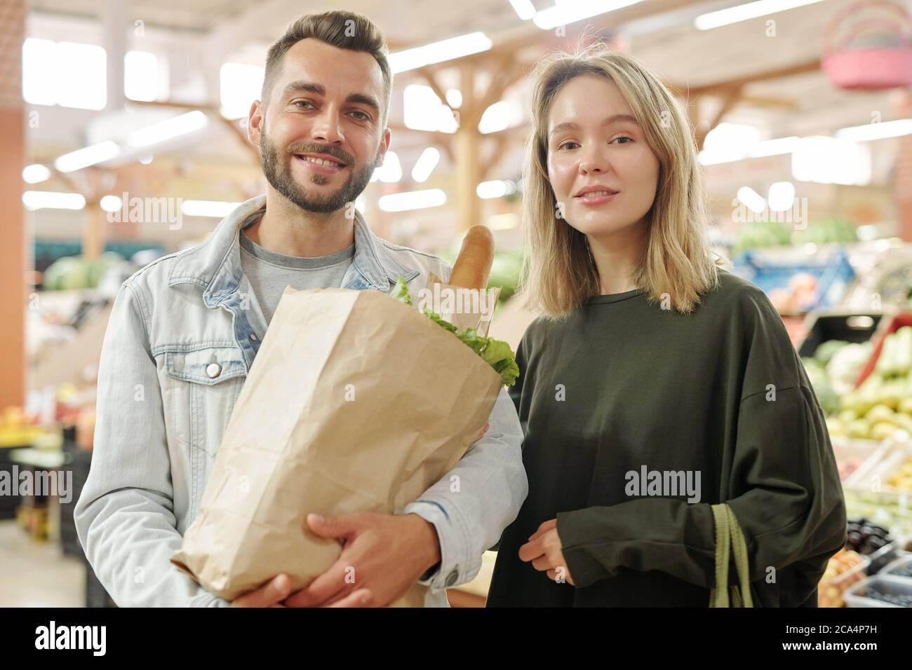 Ritratto di giovane coppia positiva in piedi al mercato agricolo e l'acquisto di cibo biologico insieme Foto Stock