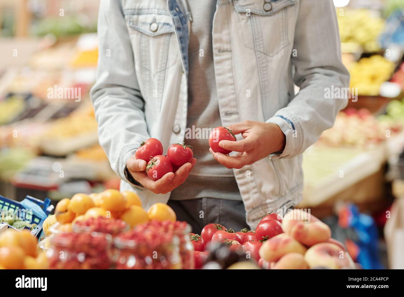 Primo piano di un uomo irriconoscibile in giacca in piedi al bancone del cibo e prendendo pomodori freschi al mercato biologico Foto Stock