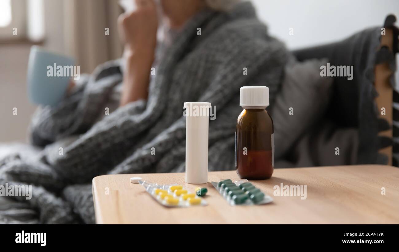 Sul comodino pillole malattia donna che tiene la tazza sullo sfondo Foto Stock