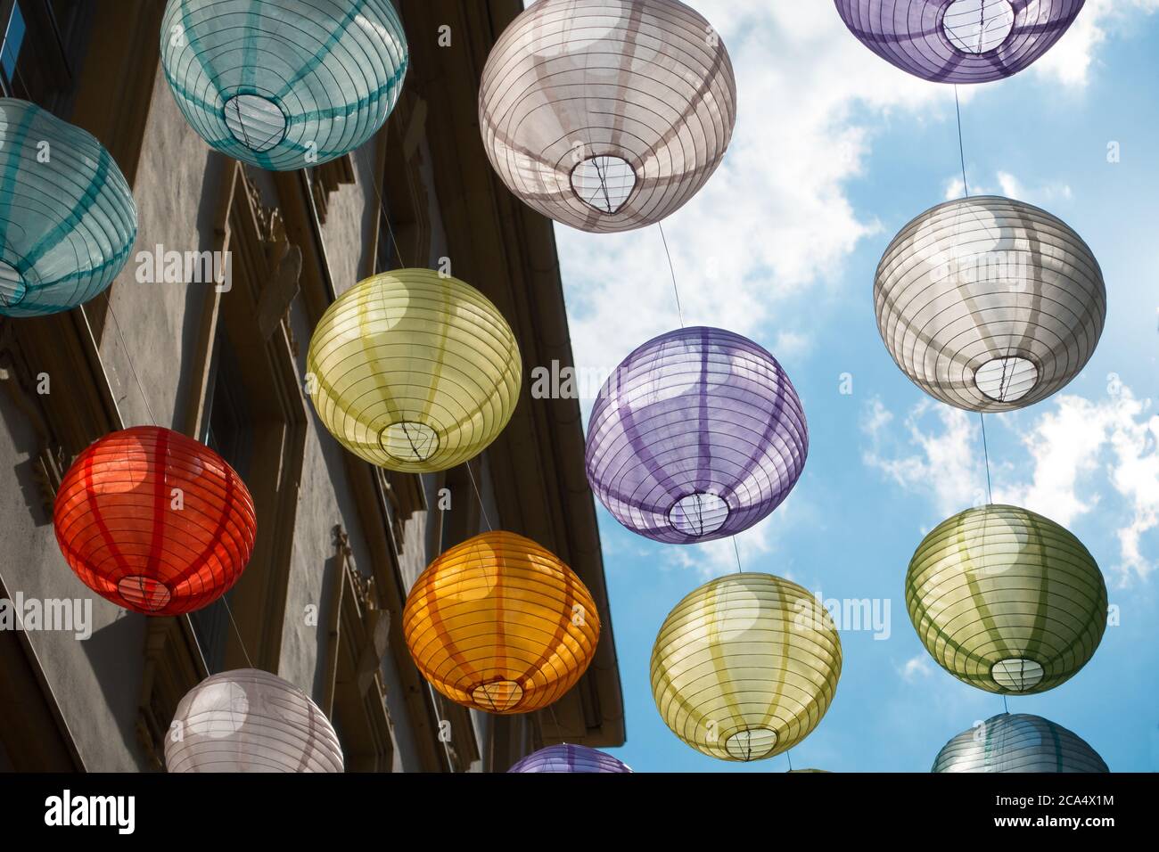 Lanterne di molti colori appendono nella città tedesca di Le decorazioni di Wurzburg sono retroilluminate contro un cielo blu in questo scena stradale vista dal basso Foto Stock