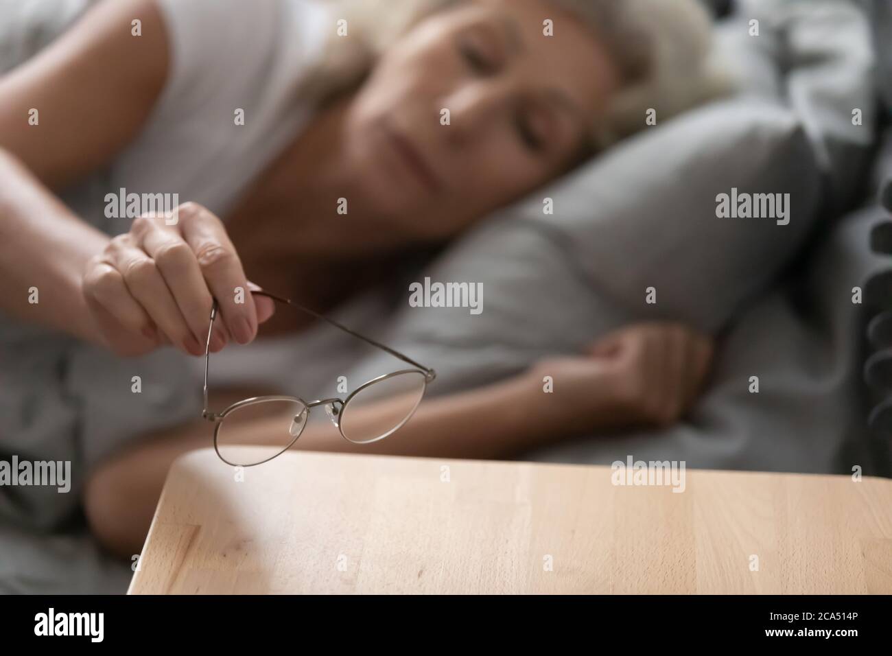 La donna anziana ha tolto gli occhiali li ha messi sul closeup del comodino Foto Stock