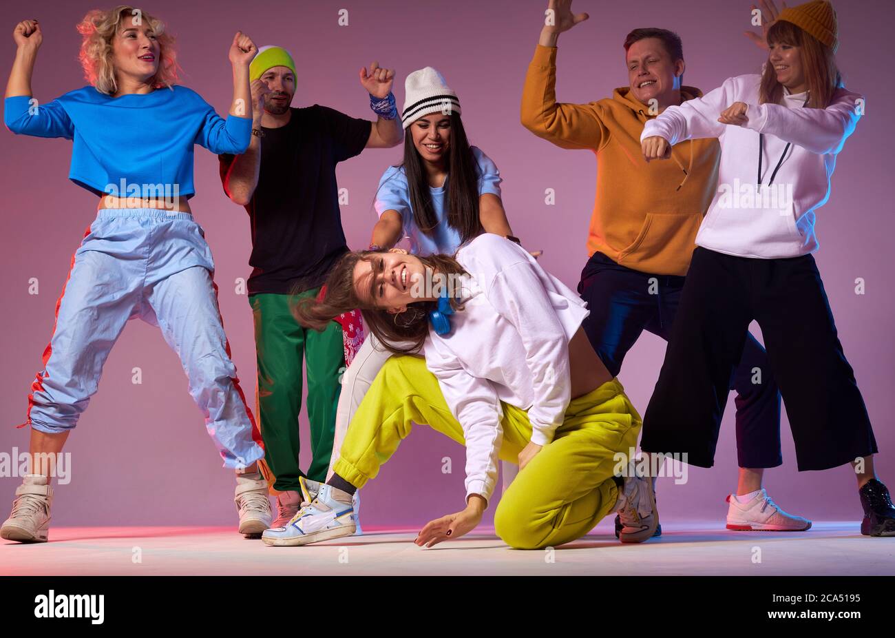 Allegri danzatori di strada sportivi che ballano attorno a una giovane donna  dai capelli ondulati seduta sul pavimento in abbigliamento sportivo,  esibendosi nel mezzo di persone urlanti Foto stock - Alamy