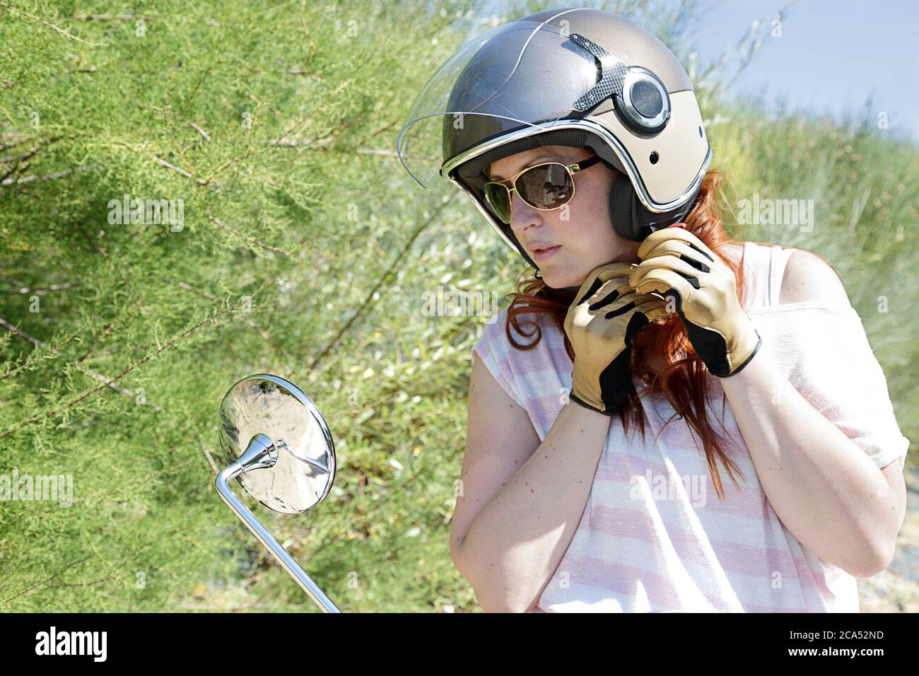 Primo piano di una giovane ragazza biker che prova su un casco di  motocicletta mentre guarda nello specchio retrovisore della sua  motocicletta Foto stock - Alamy