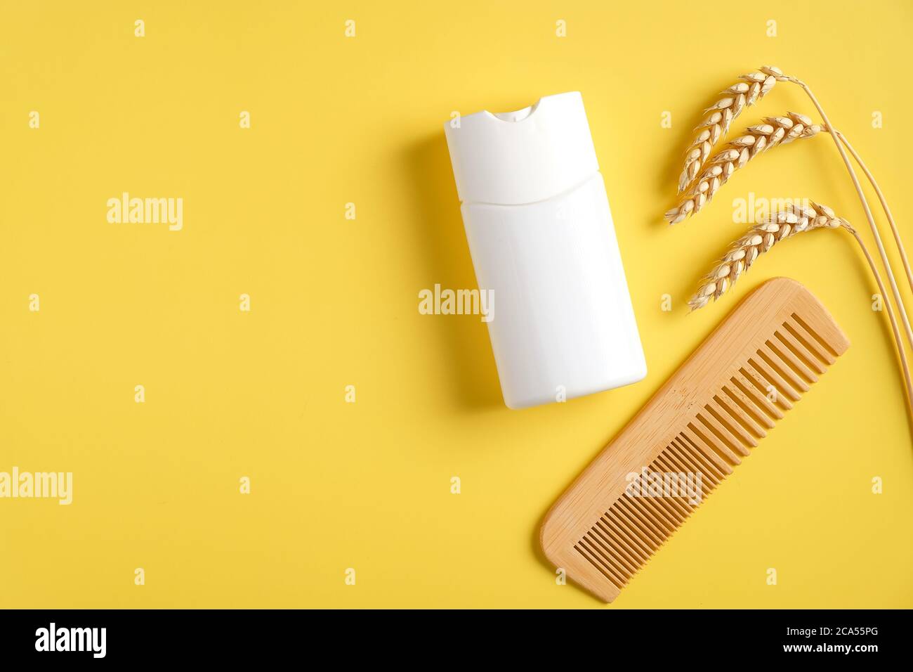 Prodotto naturale per la cura dei capelli, pettine in legno e grano su sfondo giallo. Mokup bottiglia shampoo bianco, design confezione lozione capelli. Posa piatta, parte superiore v Foto Stock