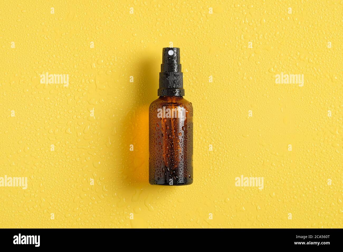 Boccetta spray in vetro ambrato bagnata con gocce d'acqua su sfondo giallo, vista dall'alto. Crema solare. Foto Stock