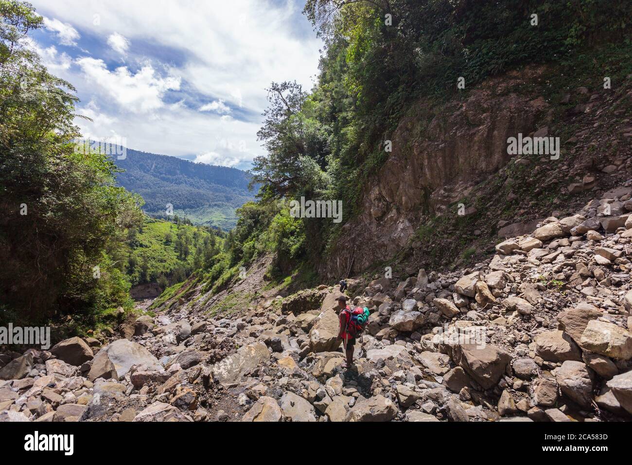 Indonesia, Papua, valle di Baliem, vicino a Walena, territorio del popolo Yali, sentieri escursionistici verso il villaggio di Angguruk, papuan facchino a piedi lungo uno scree roccioso Foto Stock