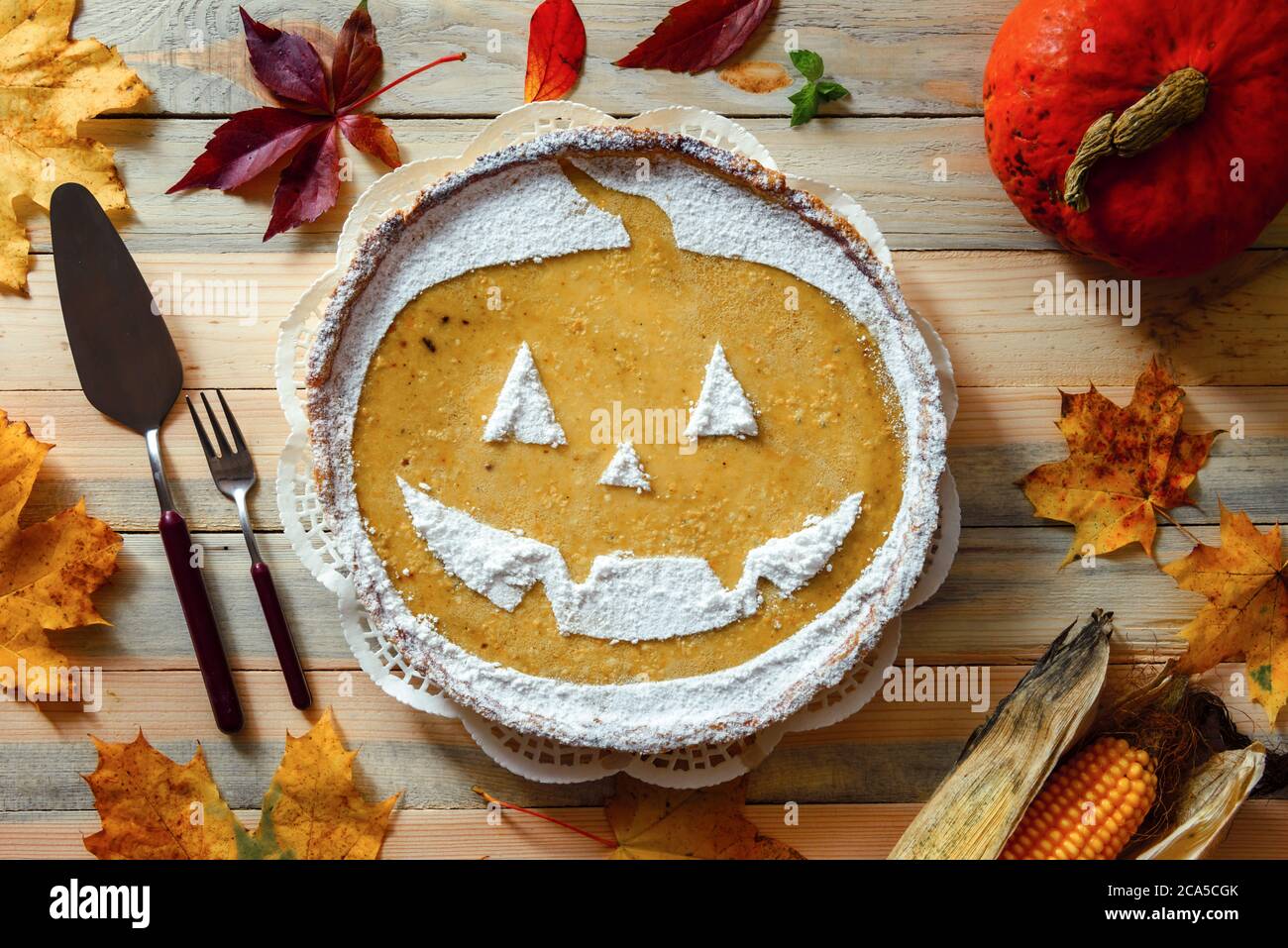 Deliziosa torta di Halloween di zucca fatta in casa con foglie di cenere e mais intorno. Dolce torta con zucchero in polvere vista dall'alto. Fotografia alimentare Foto Stock