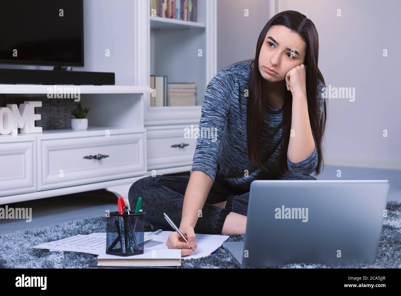 Ragazza studentesca stressata con il laptop sopravelato con la scuola e i compiti. Studentessa pensando ad un'idea. Concetto di formazione online. Concentrarsi su di lei Foto Stock