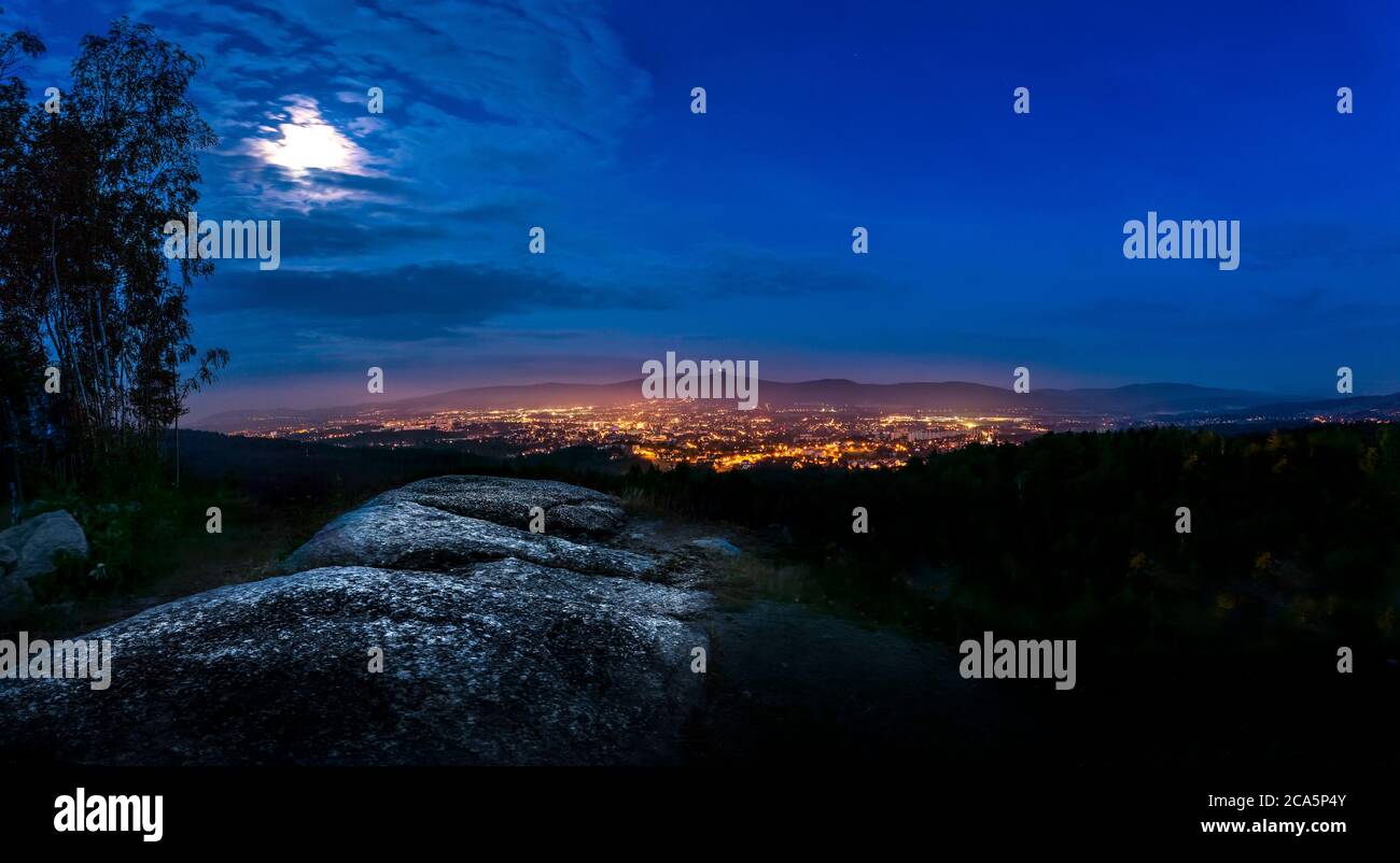 Spettacolare cielo lunare liberec con nuvole illuminate in montagna. Silhouette nera scura di cresta di montagna e torre del trasmettitore di Jested alla parte inferiore Foto Stock