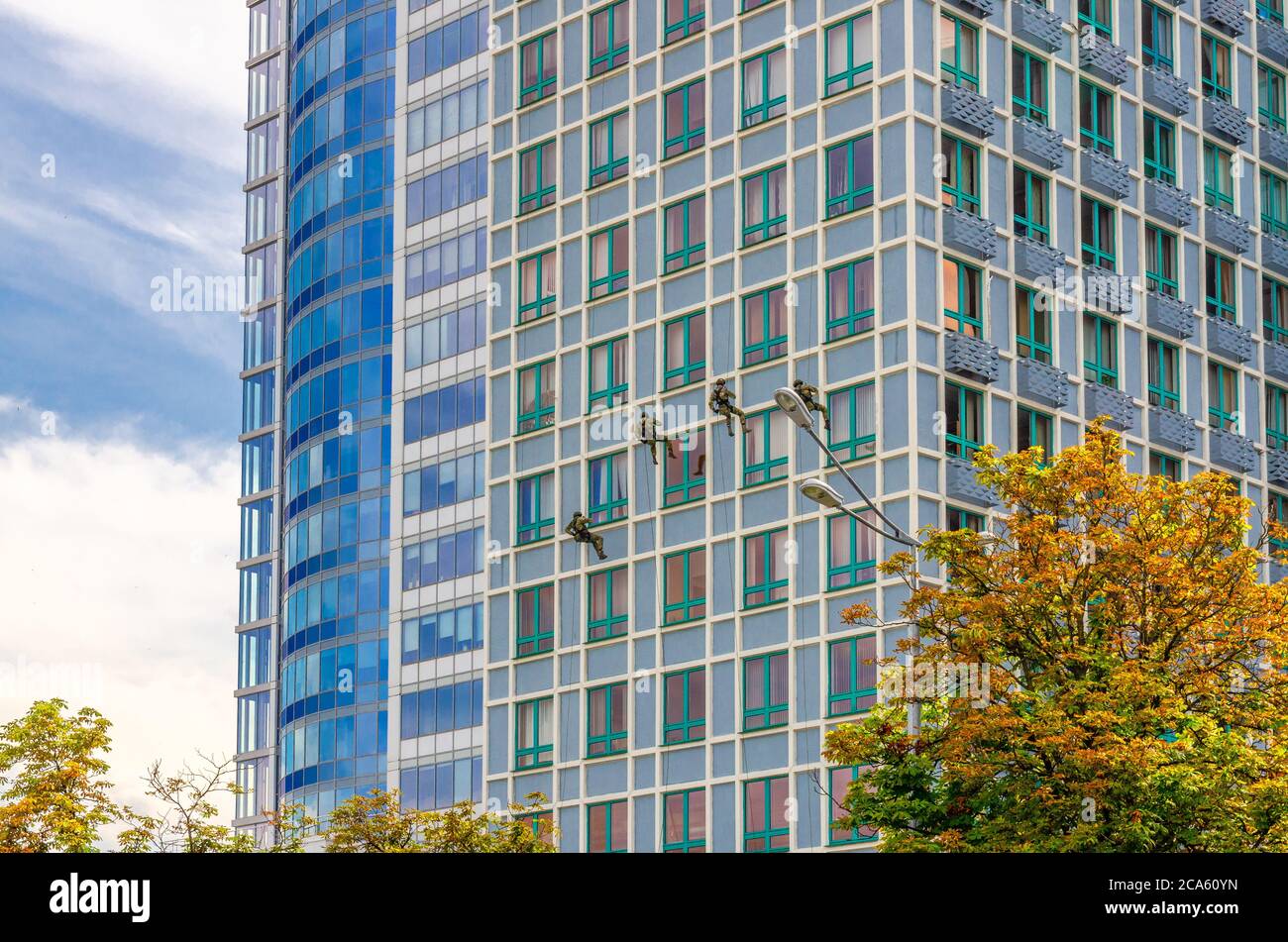 Minsk, Bielorussia, 26 luglio 2020: Soldati delle forze di operazioni speciali dell'esercito bielorusso che sale su parete di grattacieli alto edificio tra le finestre, cielo blu nuvole bianche in estate soleggiato giorno Foto Stock