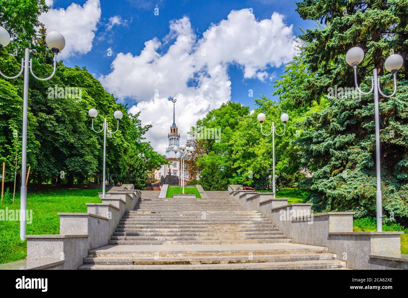 Scala in verde alberi vicolo con luci di strada, monumento della polizia e Casa sotto la guglia nel centro storico di Minsk città, cielo blu nuvole bianche in sole giorno d'estate, Repubblica di Bielorussia Foto Stock