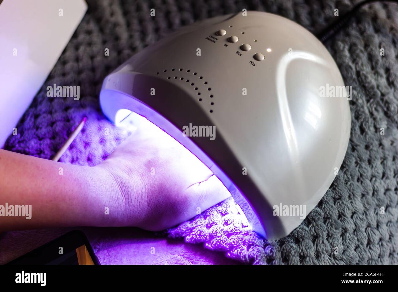 La femmina caucasica esegue l'asciugatura con smalto per unghie utilizzando la tecnica LED UV Foto Stock