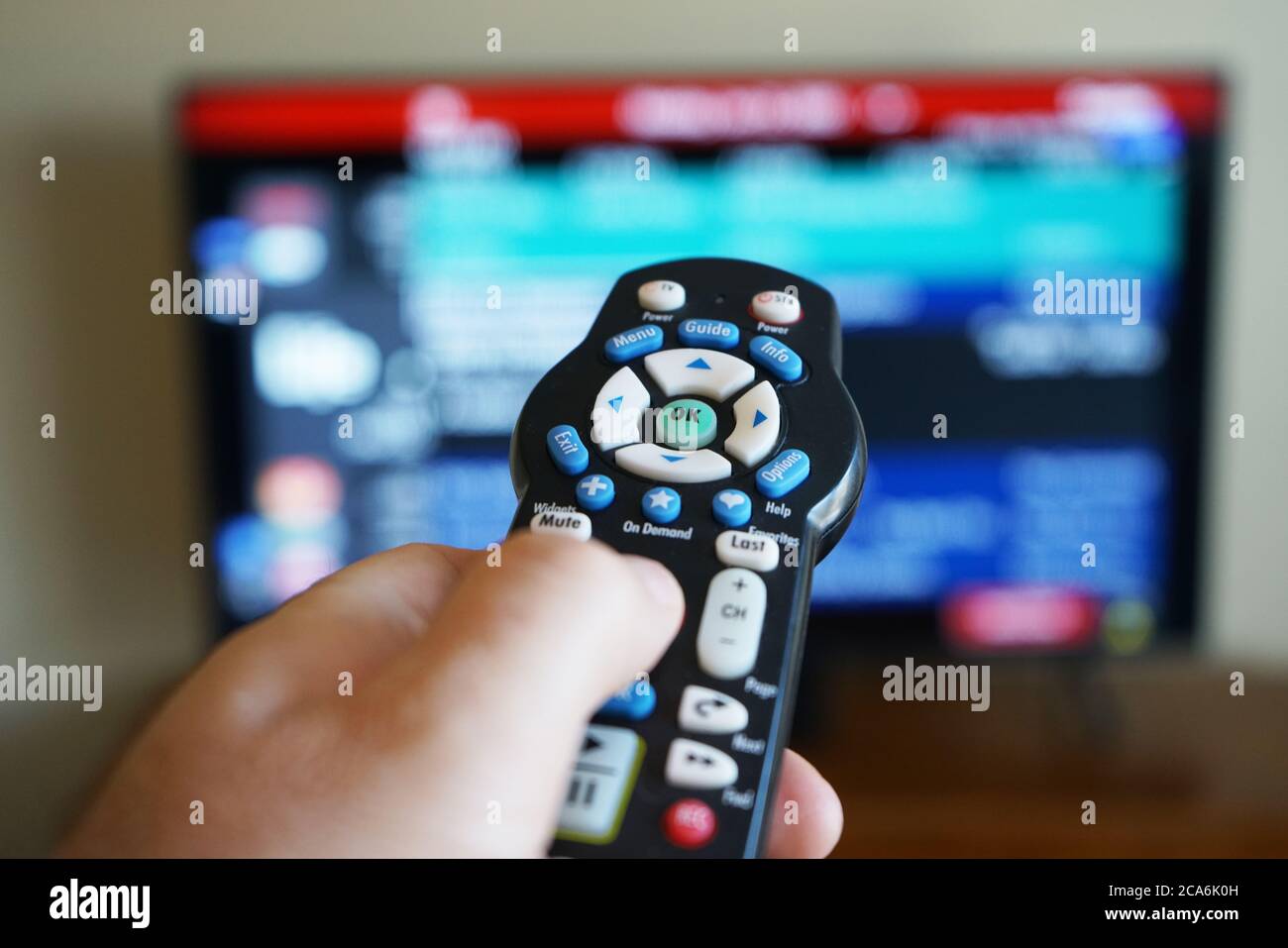 Mano che usa un telecomando TV con il televisore fuori fuoco Foto Stock