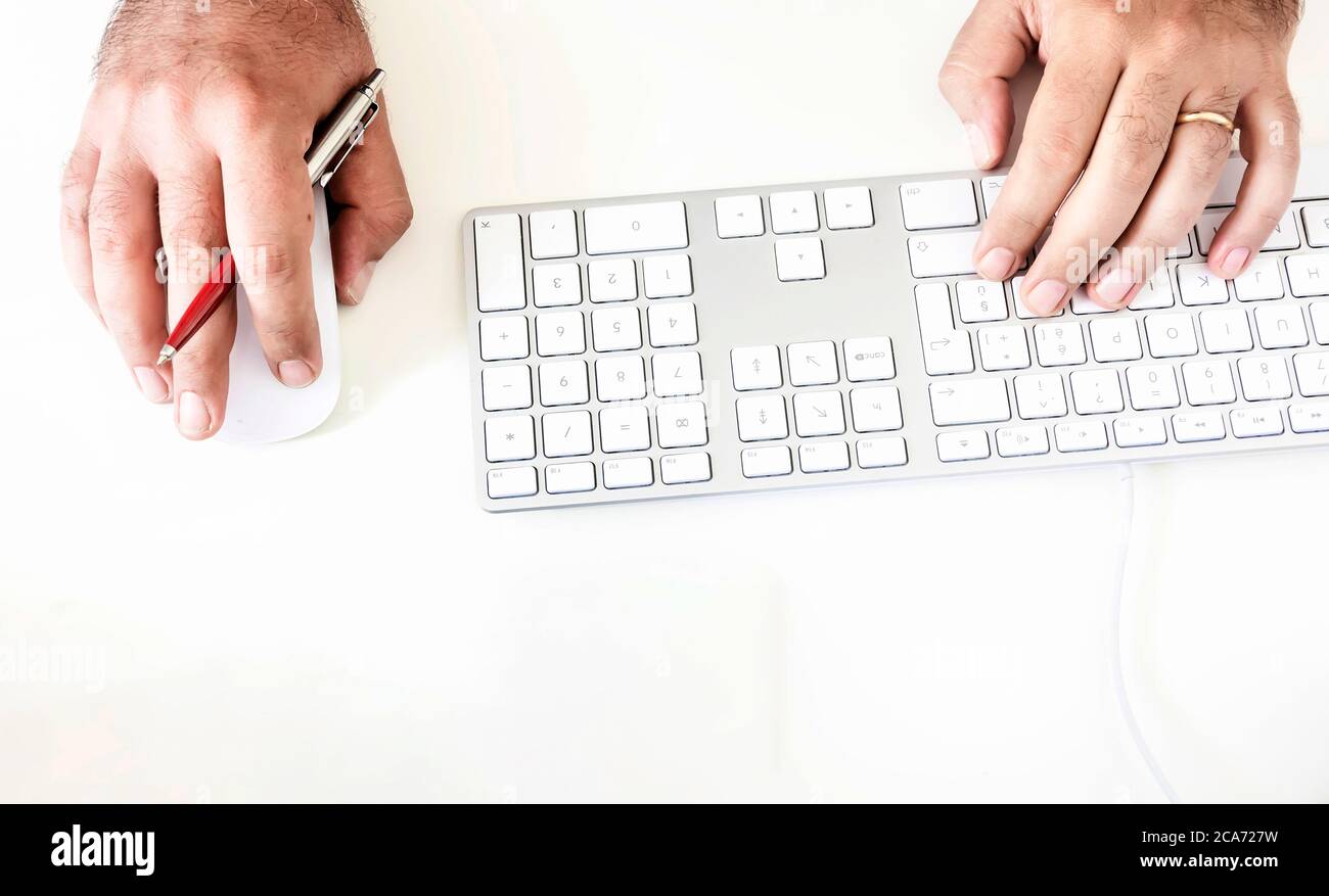 un maschio mentre usa la tastiera e il mouse del computer tenendo una penna rossa nella mano destra. Tecnologia e creatività. Lavoro creativo Foto Stock