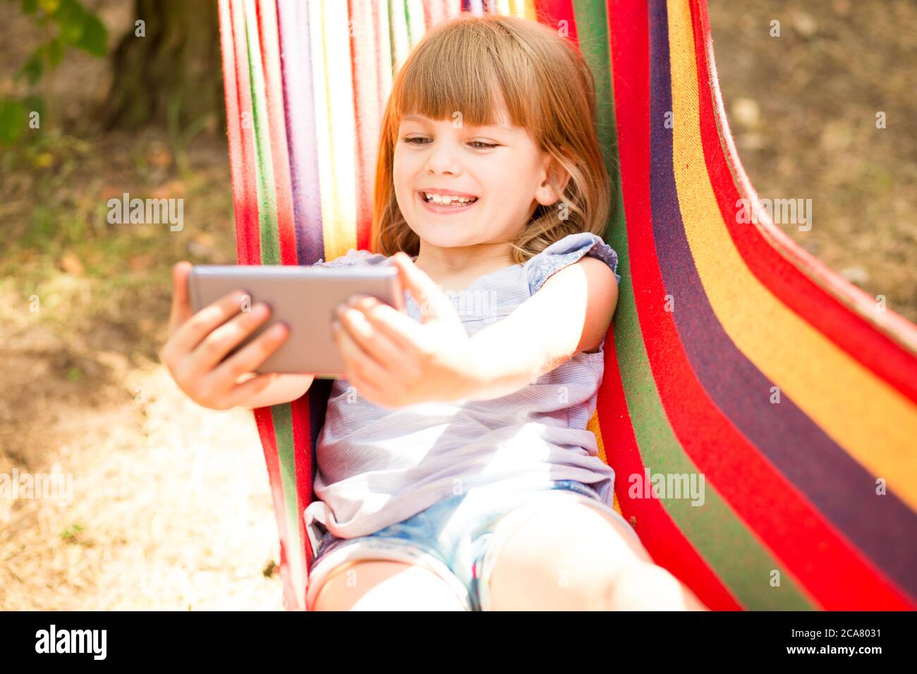 Carino bambina che cammina all'aperto e riposa su amaca in estate foresta prendendo selfie o fare videochiamata con il telefono cellulare. Foto Stock