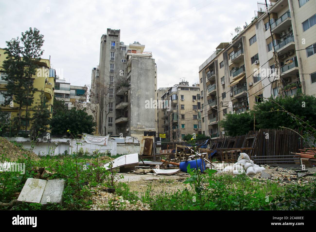Edificio danneggiato durante la guerra civile a Beirut, circondato da nuovi edifici di appartamenti, con scarti e spazzatura sull'erba di fronte agli edifici. Foto Stock