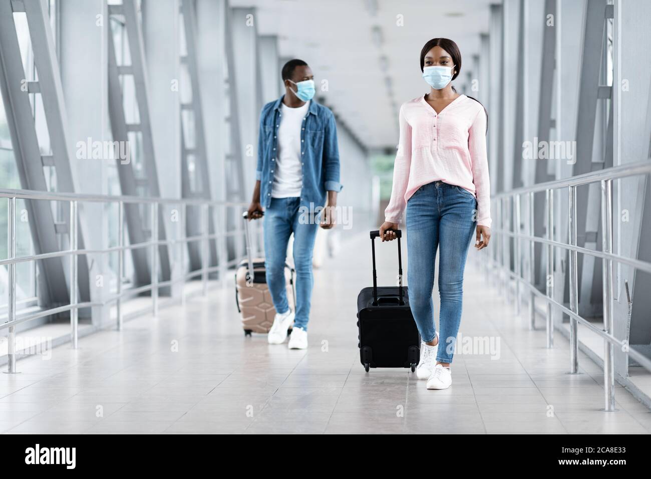 Viaggi pandemici. Black People in maschere camminare con i bagagli al terminal dell'aeroporto Foto Stock