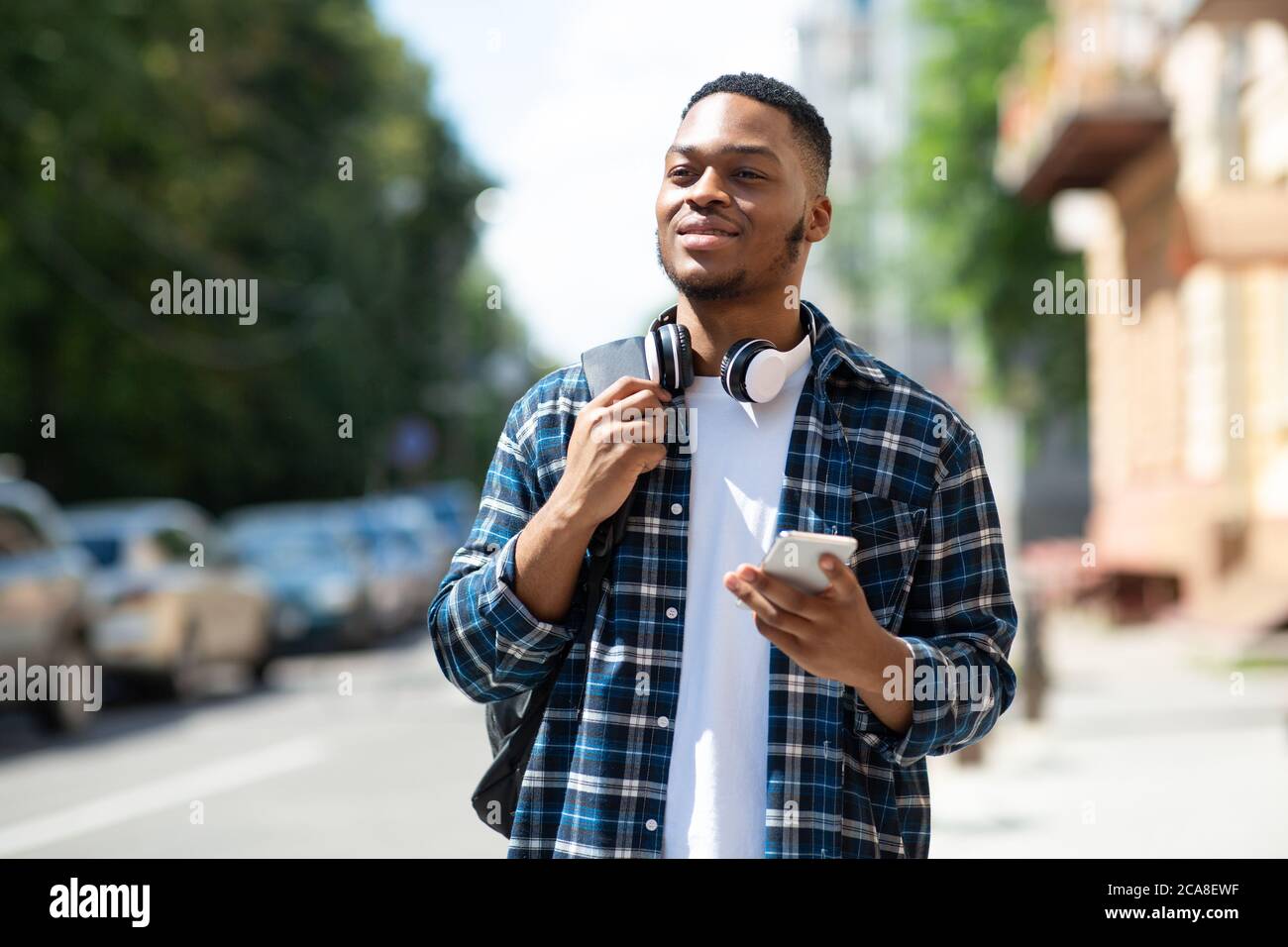 Ritratto di uomo afro che tiene il telefono, camminando giù per la strada Foto Stock