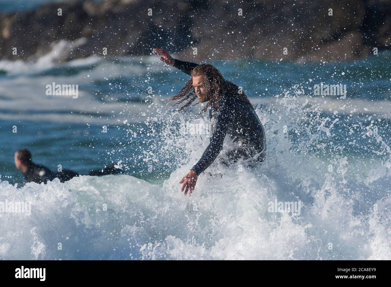 Azione spettacolare come surfista maschile con i capelli lunghi cavalca un'onda a Fistral a Newquay in Cornovaglia. Foto Stock