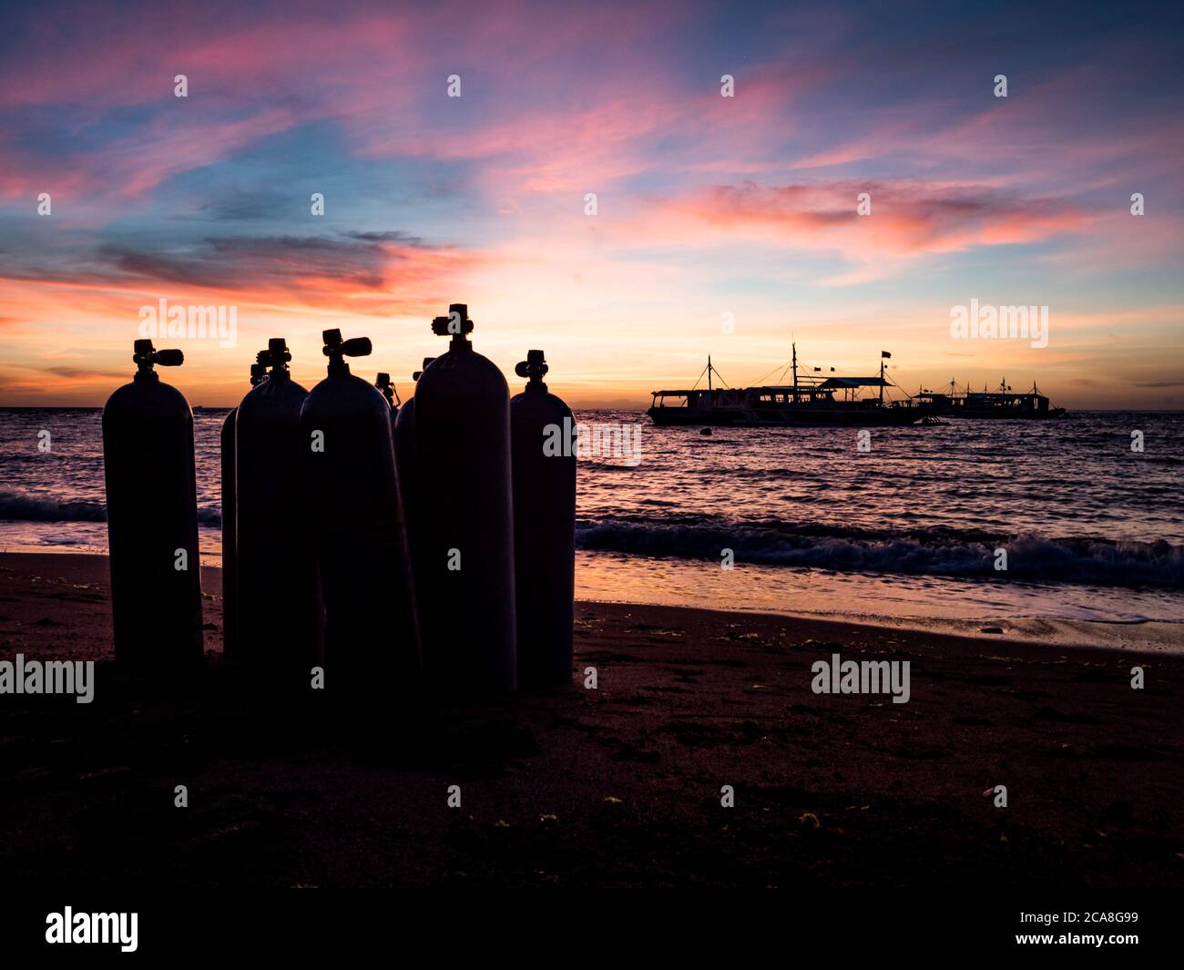 Alba sulla spiaggia nelle Filippine. Barche da immersione in attesa di subacquei al mattino presto. Silhouette di vasche da immersione in primo piano. Foto Stock