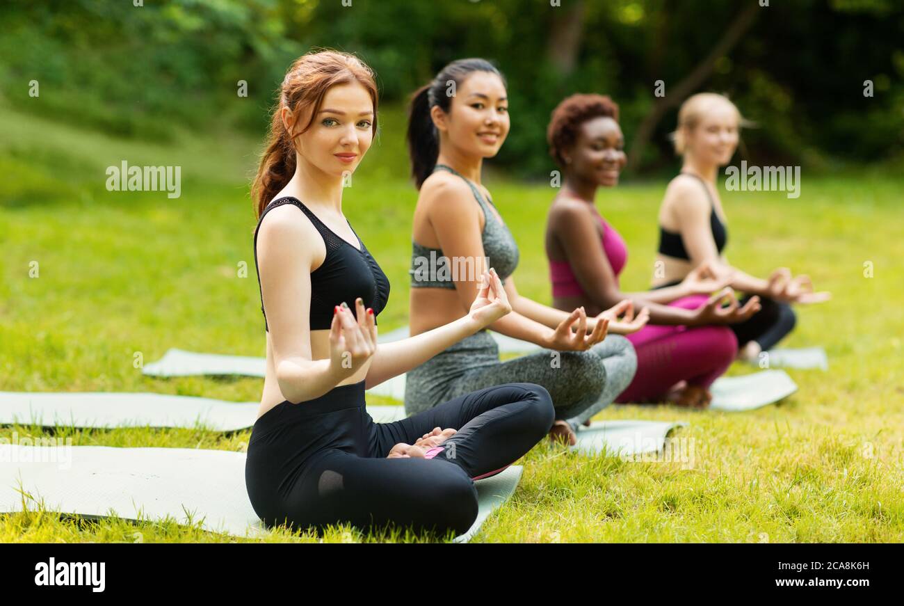 Gruppo di diverse giovani ragazze che praticano la meditazione, seduti su stuoie yoga in lotus posa all'aperto, spazio copia Foto Stock
