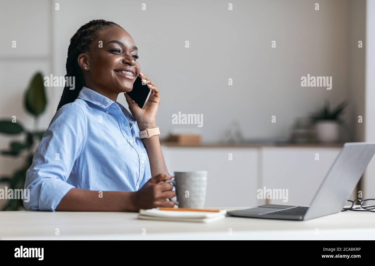 Rilassatevi al lavoro. Happy Black Segretario parlare su cellulare e bere caffè Foto Stock