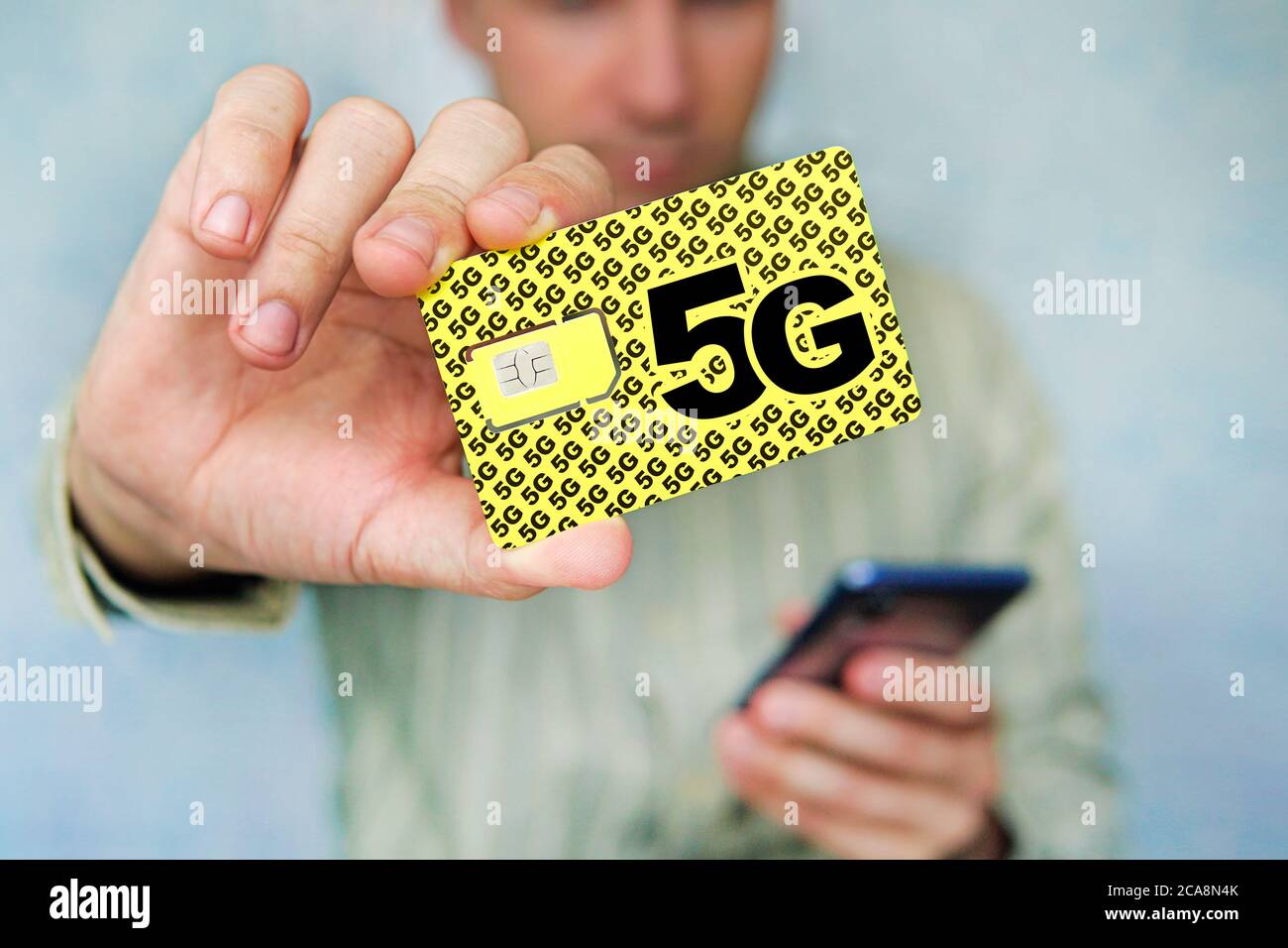 L'uomo tiene una carta SIM gialla con l'iscrizione 5G e un telefono cellulare in mano. Sostituzione della scheda SIM e passaggio a Internet ad alta velocità. Foto Stock