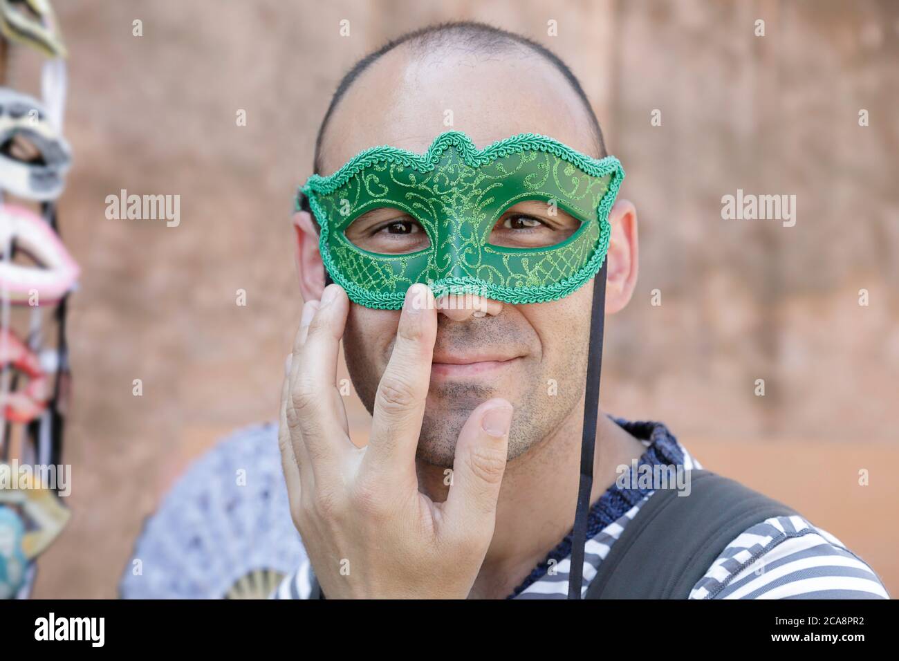 Uomo che prova su una maschera di carnevale veneziana accanto a un stand di strada Foto Stock