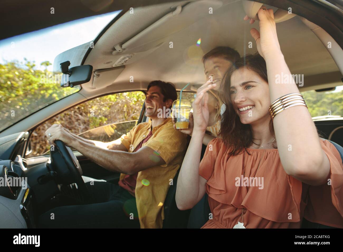 Sorridente famiglia con bambini seduti in auto e alla guida. La famiglia si diverte durante il viaggio. Foto Stock