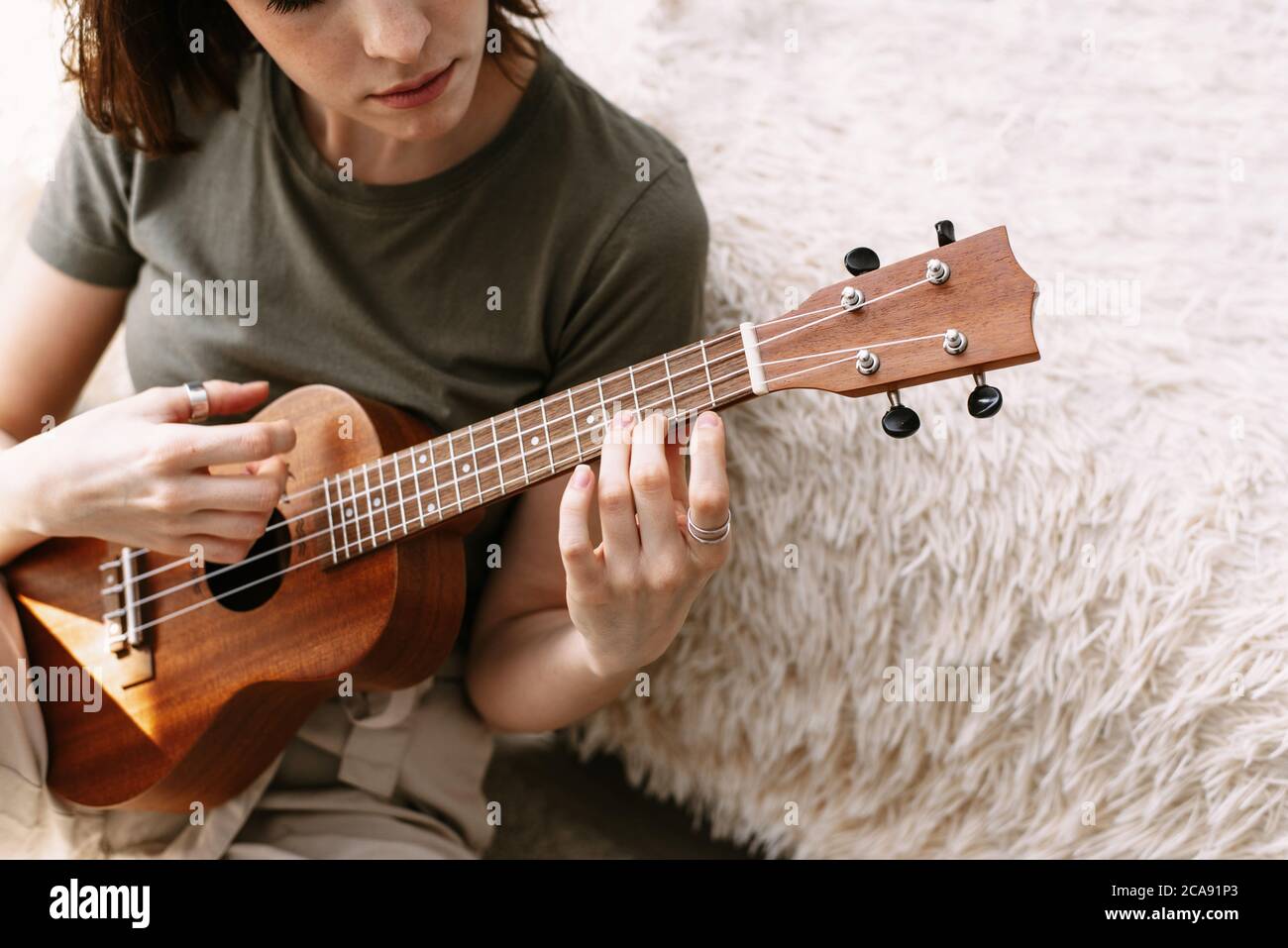 Una bella donna suona la piccola chitarra a casa. Una giovane ragazza gioca  ukulele durante l'isolamento Foto stock - Alamy