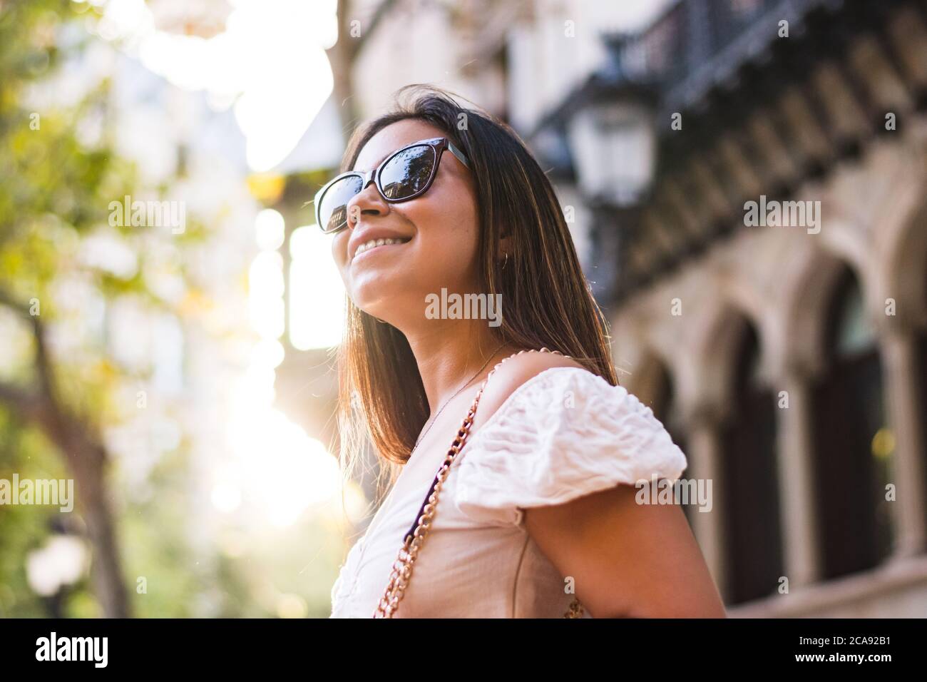 donna con occhiali da sole sorride mentre cammina per la città Foto Stock