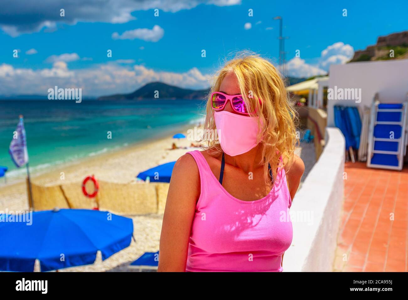 Donna lifestyle con maschera chirurgica rosa sulla terrazza sul tetto a le Ghiaie Beach durante la pandemia di Covid-19, isola d'Elba, Toscana, Italia, Europa Foto Stock